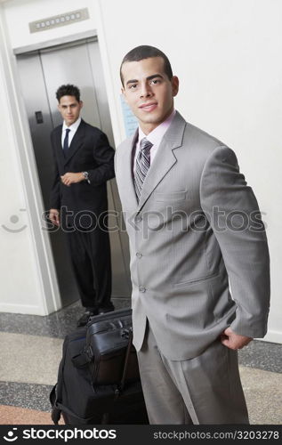 Portrait of a businessman with luggage and a businessman standing in front of an elevator