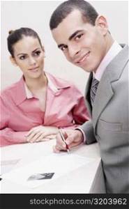 Portrait of a businessman writing on paper and a businesswoman standing beside him