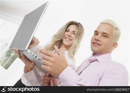 Portrait of a businesswoman and a businessman using a laptop and smiling