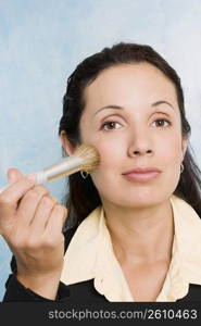 Portrait of a businesswoman applying make-up on her face with a make-up brush