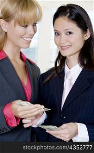 Portrait of a businesswoman giving a dollar bill to another businesswoman