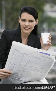 Portrait of a businesswoman holding a disposable cup and a newspaper