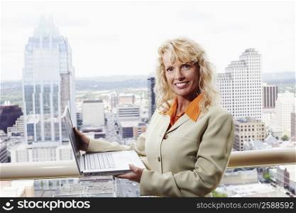 Portrait of a businesswoman holding a laptop with buildings in the background