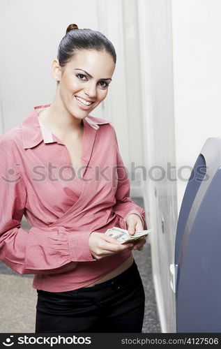 Portrait of a businesswoman holding paper currency in front of an ATM