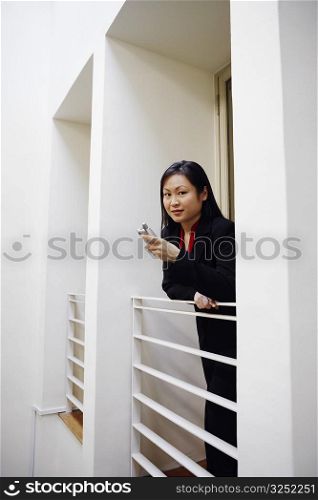 Portrait of a businesswoman leaning over a railing and holding a mobile phone