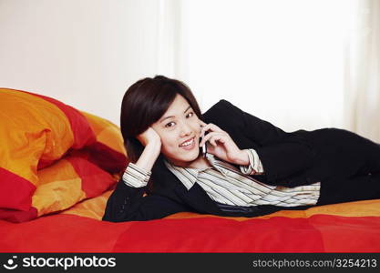 Portrait of a businesswoman lying on the bed and talking on a mobile phone