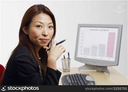 Portrait of a businesswoman sitting in front of a computer and holding a pen