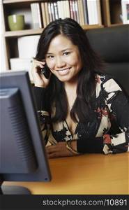 Portrait of a businesswoman sitting in front of a computer monitor using a mobile phone