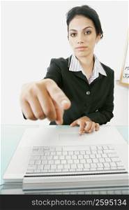 Portrait of a businesswoman sitting in front of a laptop and pointing forward