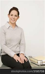 Portrait of a businesswoman sitting on a desk and smiling