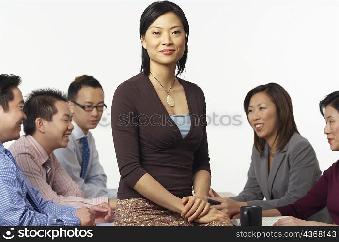 Portrait of a businesswoman sitting on a table with business executives sitting behind her
