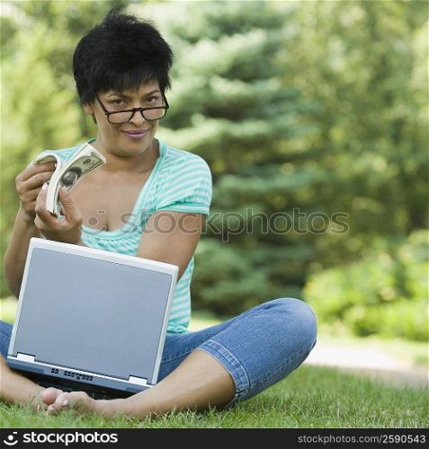 Portrait of a businesswoman sitting with a laptop and holding a wad of currency