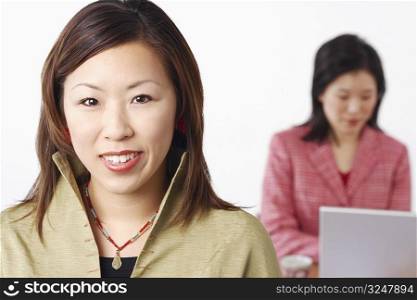 Portrait of a businesswoman smiling with another businesswoman using a laptop behind her