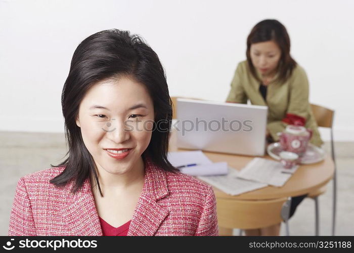 Portrait of a businesswoman smiling with another businesswoman using a laptop behind her