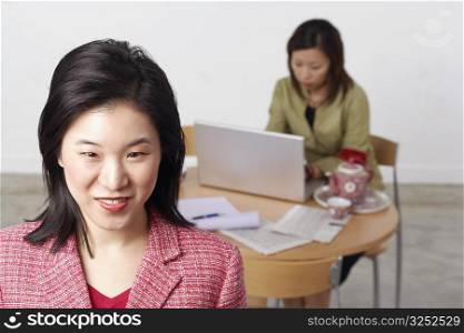 Portrait of a businesswoman smiling with another businesswoman using a laptop behind her