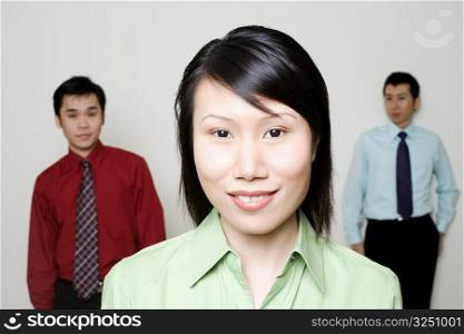Portrait of a businesswoman smiling with two businessmen standing behind her