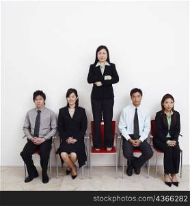 Portrait of a businesswoman standing on an armchair with four business executives sitting beside her