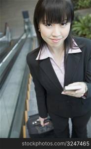 Portrait of a businesswoman standing on an escalator and holding a mobile phone