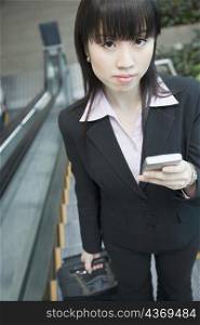 Portrait of a businesswoman standing on an escalator and holding a mobile phone