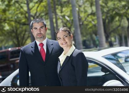 Portrait of a businesswoman standing with a businessman in front of a car