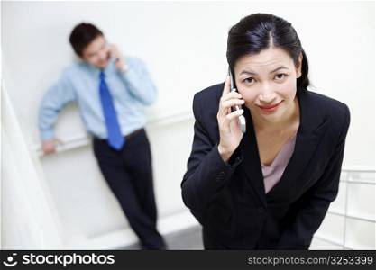 Portrait of a businesswoman talking on a mobile phone with a businessman standing behind her
