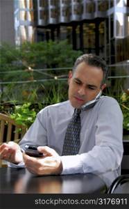 Portrait of a busy businessman in the city using pda and cell phone