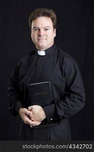 Portrait of a catholic priest holding the bible. Black background.