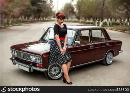 portrait of a Caucasian beautiful young girl in a black vintage dress, posing near a vintage car