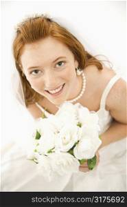 Portrait of a Caucasian bride holding bouquet looking up towards viewer.