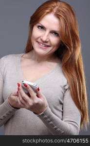 Portrait of a charming young female text messaging on cellphone against grey background