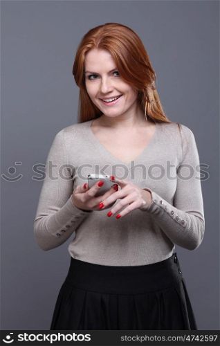 Portrait of a charming young female text messaging on cellphone against grey background