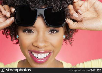 Portrait of a cheerful African American woman holding sunglasses over colored background