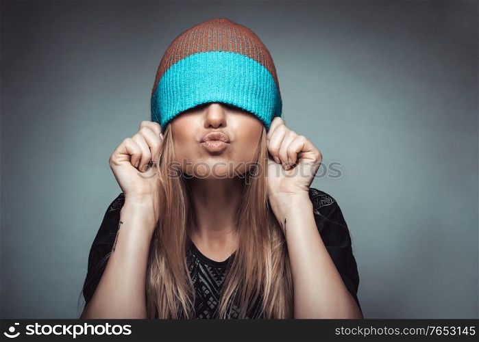 Portrait of a cheerful girl wearing a hat on her face and showing kiss, playing and having fun, concept of enjoying life, youth funky fashion