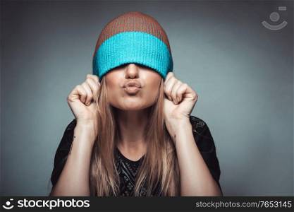 Portrait of a cheerful girl wearing a hat on her face and showing kiss, playing and having fun, concept of enjoying life, youth funky fashion