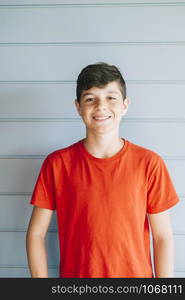 Portrait of a cheerful male teen leaning on wood wall while looking camera in a sunny day