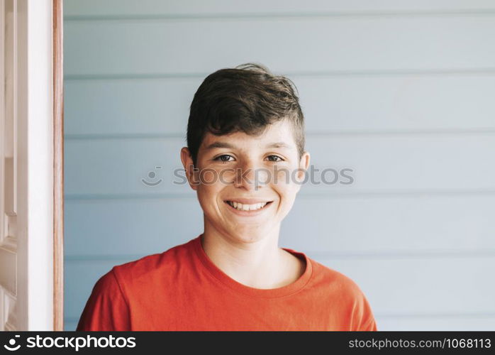 Portrait of a cheerful male teen leaning on wood wall while looking camera in a sunny day