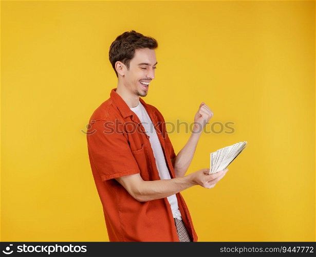 Portrait of a cheerful man holding dollar bills and doing winner gesture clenching fist over yellow background. Finance, investment and money saving concept.