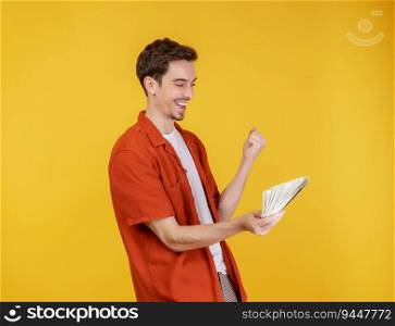 Portrait of a cheerful man holding dollar bills and doing winner gesture clenching fist over yellow background. Finance, investment and money saving concept.