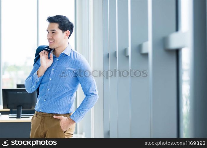 Portrait of a cheerful mature asian young businessman wear a business suit of man in blue jacket and blue shirt looking at the window In the office room background.