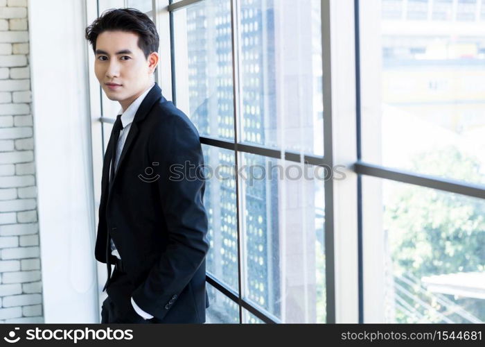 Portrait of a cheerful mature asian young businessman wear a business suit of man in blue jacket and blue shirt looking at the window In the office room background.