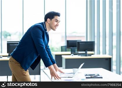 Portrait of a cheerful mature asian young businessman wear a business suit of man in blue shirt and laptop looking at the window In the office room background.