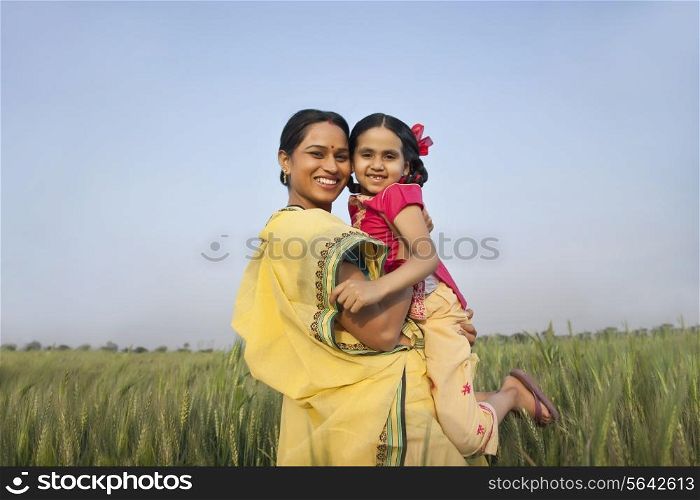 Portrait of a cheerful mother carrying daughter against clear sky in a wheat field