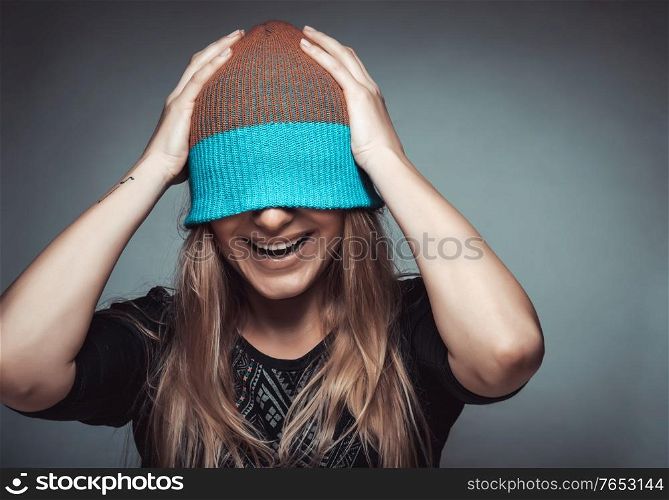 Portrait of a cheerful smiling female student wearing a hat on her face, playing and having fun, concept of enjoying life, funky youth, street urban style fashion for youngsters