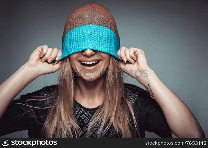 Portrait of a cheerful smiling young woman wearing a hat on her face, playing and having fun, concept of enjoying of life, youth, funky fashion