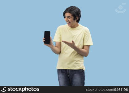 Portrait of a cheerful teenage boy holding a Smartphone and gesturing against blue background