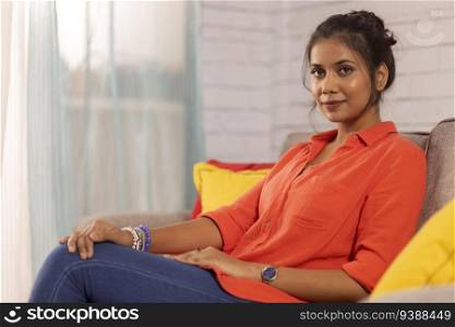 Portrait of a cheerful woman looking at camera while relaxing on sofa in living room