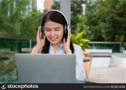 Portrait of a cheerful young attractive Asian woman listening music and using laptop computer for working online. Distance learning online education and work via the internet. Successful people