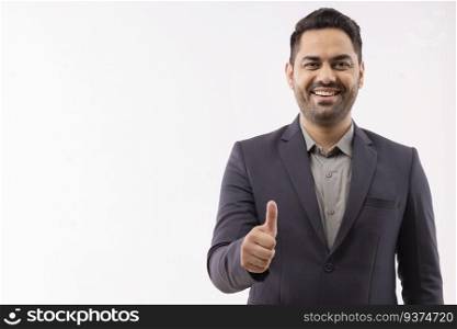 Portrait of a cheerful young businessman in formal outfit showing thumbs up gesture
