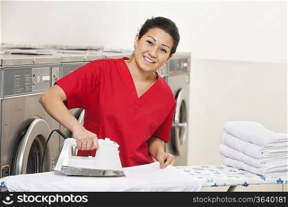 Portrait of a cheerful young employee ironing in Laundromat