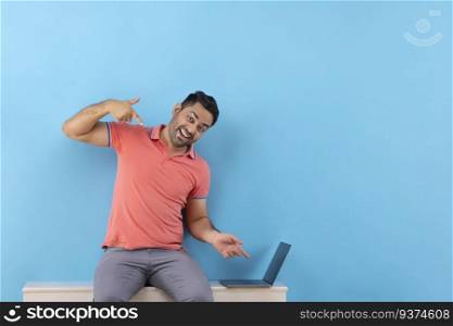 Portrait of a cheerful young man looking at camera and pointing at his laptop